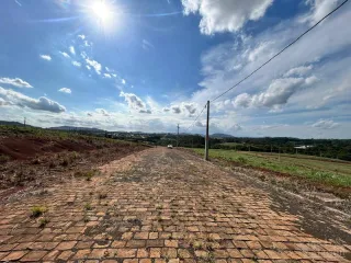 Vista de uma estrada de terra em uma área rural sob um céu azul com nuvens.