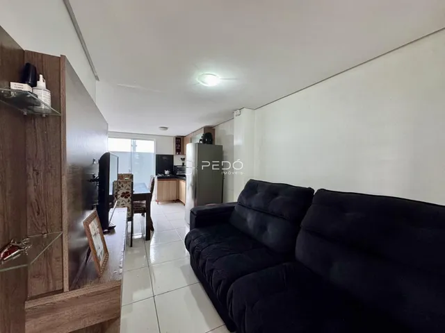 Sala de estar com sofá preto e passagem para a cozinha