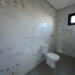 Foto de um banheiro com parede de mármore branco e vaso sanitário.