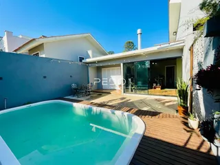 Foto da fachada de uma casa com piscina e deck de madeira.