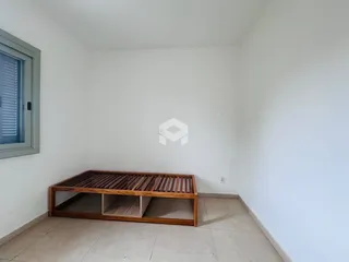 Quarto vazio com parede branca e cama de madeira no interior da propriedade.