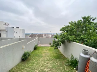 Quintal gramado cercado por um muro alto e vegetação.