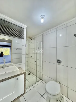 Banheiro com revestimento cerâmico branco e piso claro.