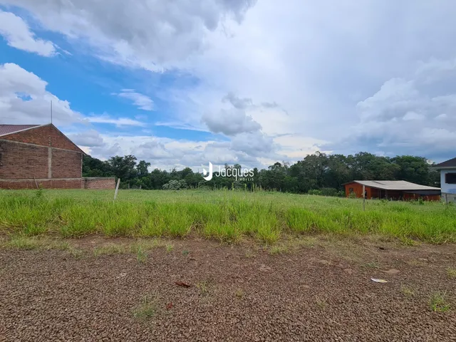 Campo de grama verde com construções rurais ao fundo.