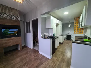 Interior de uma sala de estar com piso de madeira e cozinha moderna.