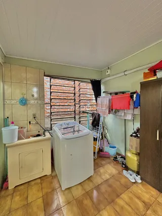 Imagem de uma área de serviço com máquina de lavar e janela de tijolos aparentes.