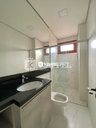 Banheiro com bancada escura e box de vidro transparente.