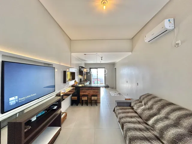 Sala de estar moderna com cozinha integrada e televisão.
