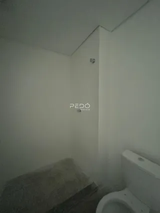 Vista interna de um corredor com parede branca e vaso sanitário.