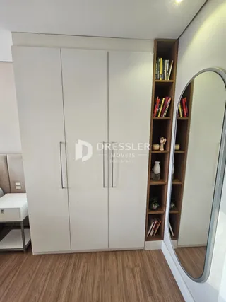 Quarto com armários brancos e espelho grande.