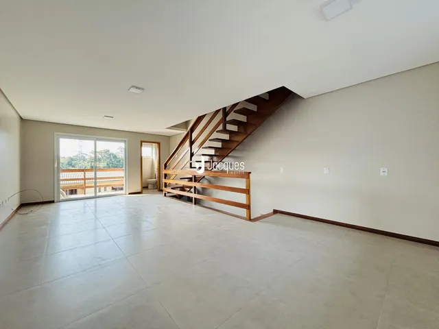 Ambiente interno de uma sala ampla com piso de porcelanato e escadaria de madeira.