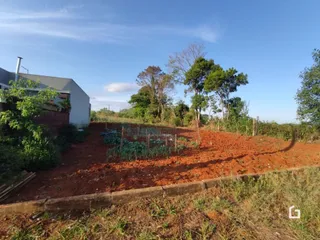 Vista externa de um terreno com solo avermelhado e vegetação rasteira.