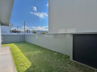 Vista externa de um quintal gramado com muro branco e porta de garagem.