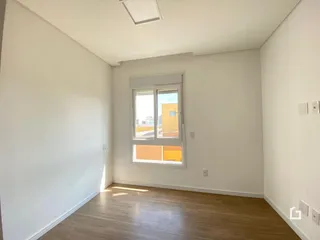 Ambiente interno de uma sala com piso de madeira clara e paredes brancas.