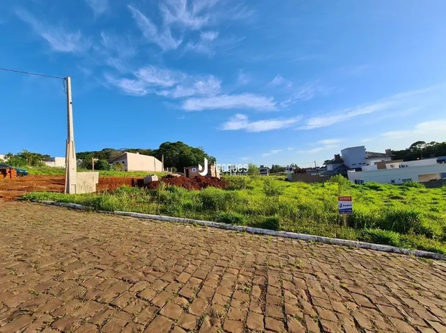 Vista externa de uma propriedade com área gramada e pavimentação de paralelepípedos.