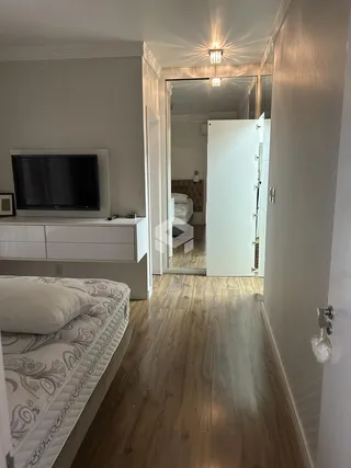 Quarto com piso de madeira e televisão em um apartamento em Lajeado.