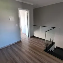 Ambiente interno com piso de madeira e guarda-corpo de vidro.