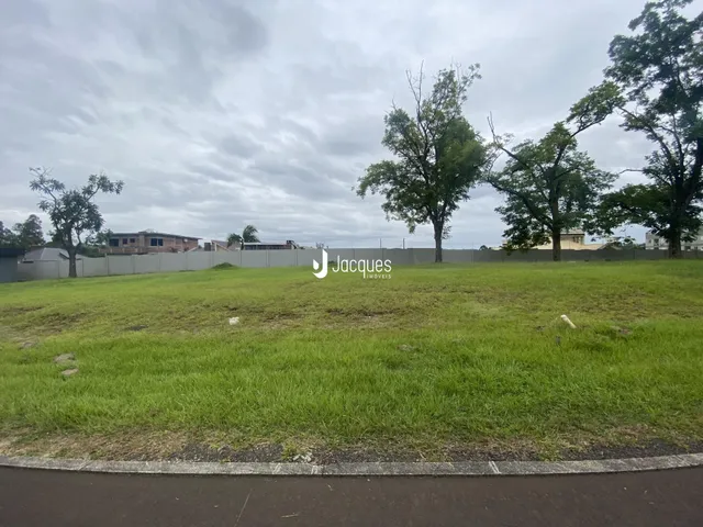 Vista externa de um terreno gramado com árvores e cerca.