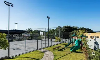 Vista externa de um campo esportivo cercado por cerca e área gramada.