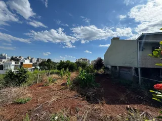 Vista externa da propriedade mostrando terreno seco e vegetação no primeiro plano com um edifício ao fundo.