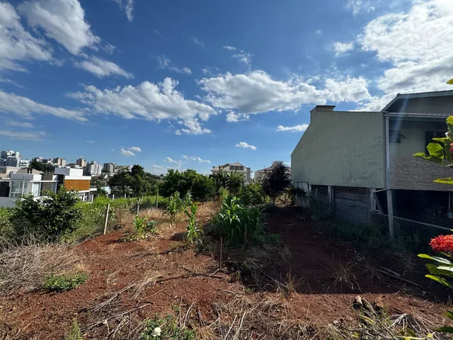 Vista externa da propriedade mostrando terreno seco e vegetação no primeiro plano com um edifício ao fundo.