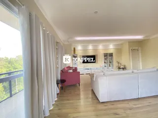 Sala de estar com sofá branco e piso de madeira clara, com grande janela para a paisagem.