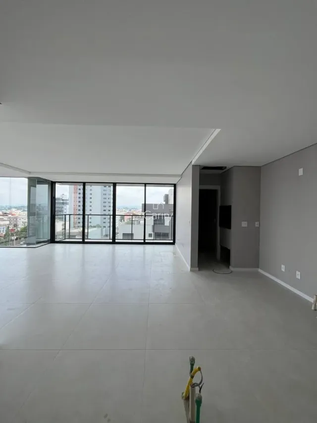 Ambiente interno amplo com piso claro e grandes janelas que oferecem vista.
