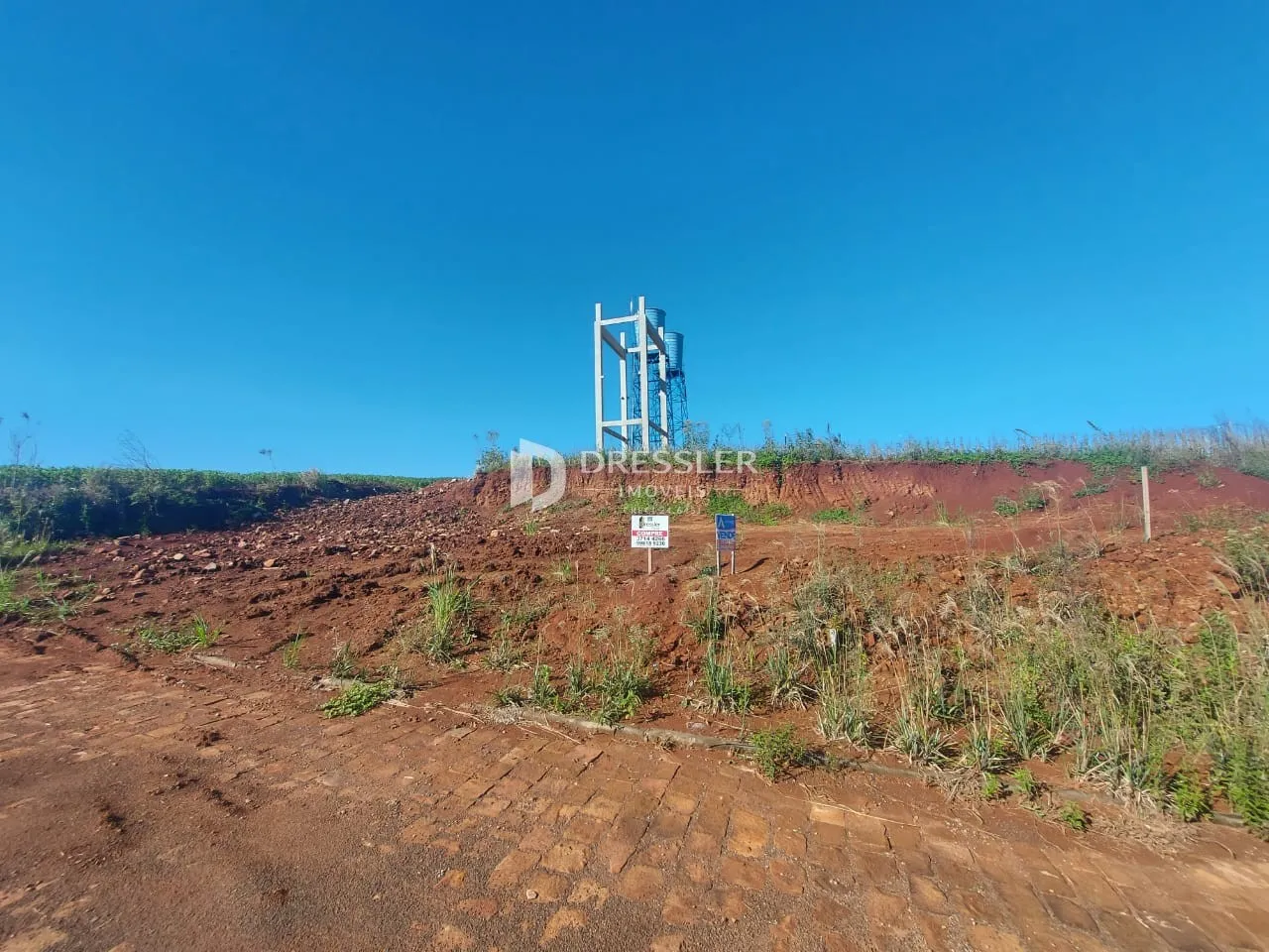 Paisagem de terra vermelha com uma estrutura metálica no fundo sob um céu azul.