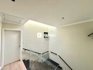 Hall de entrada com escadaria de vidro e piso de madeira.