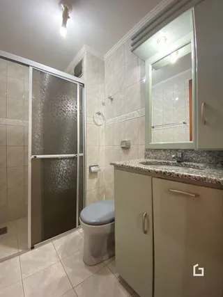 Interior de um banheiro com revestimento cerâmico e box de vidro.