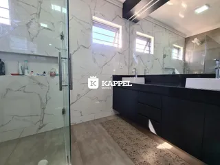 Banheiro com revestimento de mármore branco e bancada escura.