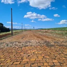 Vista de uma estrada de terra estendendo-se por um campo aberto sob um céu azul com nuvens.