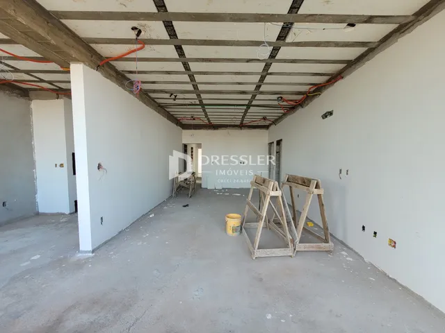 Interior de um espaço em construção com vigas expostas e paredes brancas.