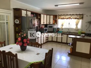 Uma mesa de jantar coberta com toalha branca está posicionada em uma sala com armários de madeira.