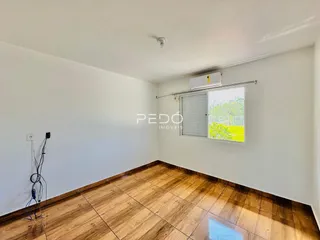 Ambiente interno de uma sala com piso de madeira e paredes brancas.