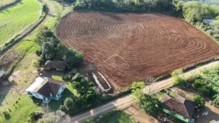 Vista aérea de uma propriedade rural com campo cultivado e uma casa no primeiro plano.