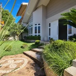 Jardim externo com grama e vegetação na frente da residência.