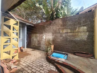 Vista externa de um pátio com parede de alvenaria rústica e piso de tijolos.