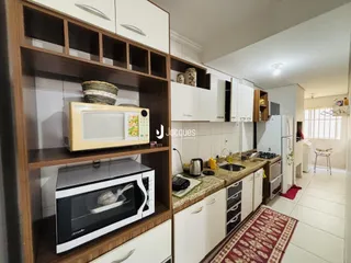 Vista interna de uma cozinha com armários brancos e prateleiras de madeira.
