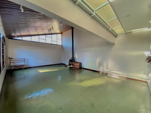 Esta é uma sala ampla com piso verde e teto com claraboia.
