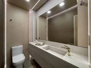 Interior de um banheiro moderno com bancada de mármore e louças brancas.