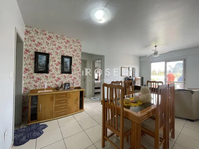 Ambiente interno de uma sala com mesa de jantar de madeira e papel de parede floral.