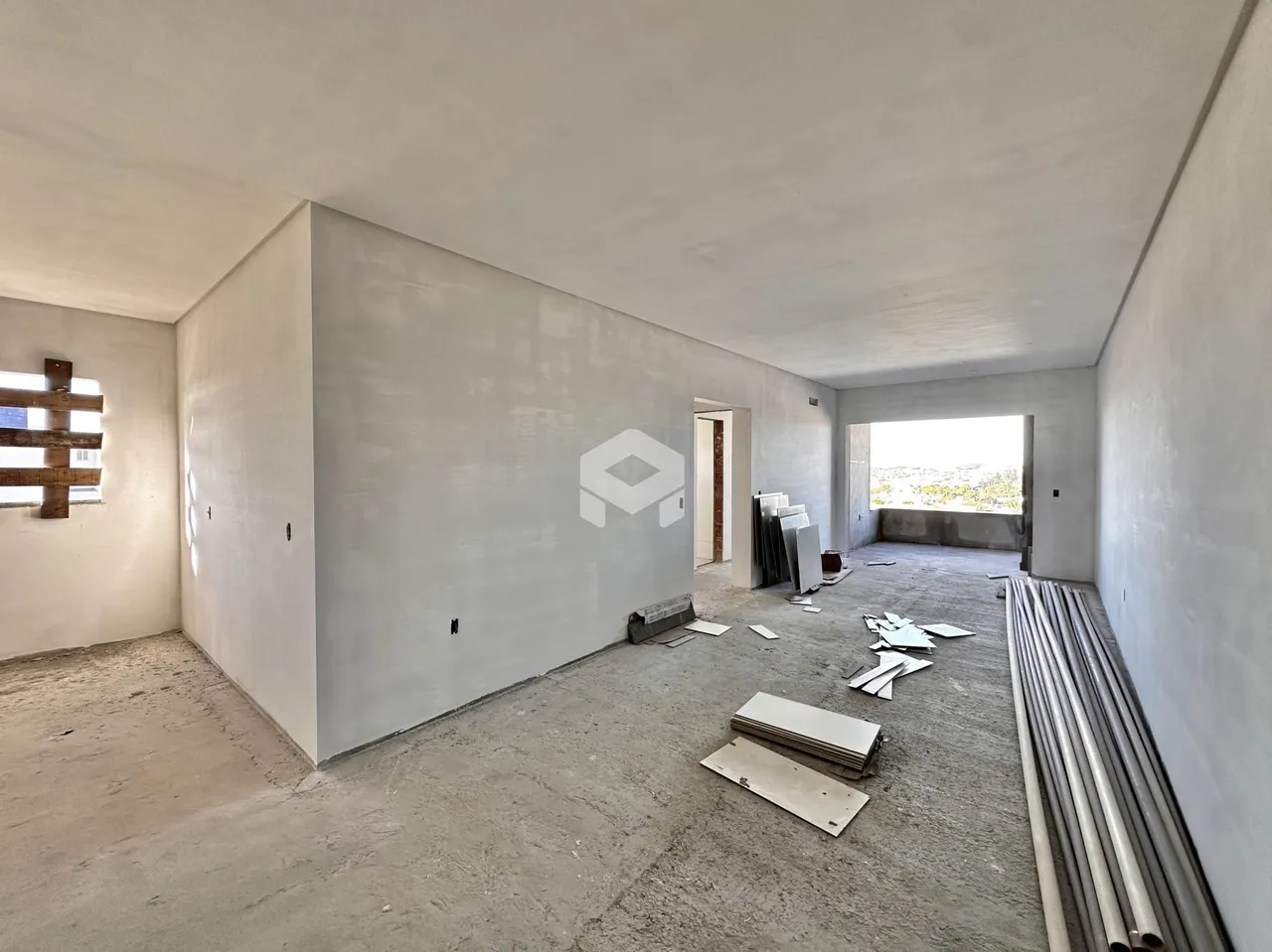 Interior de um cômodo em construção com paredes brancas e piso de concreto.