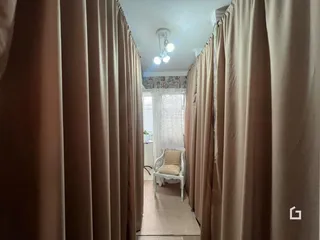 Corredor interno com cortinas bege e uma cama ao fundo.