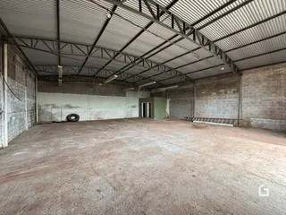 Interior de um grande espaço industrial com teto de metal e paredes de concreto.