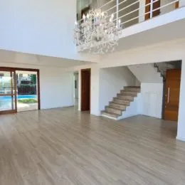 Ambiente interno amplo com piso de madeira e escadaria visível.