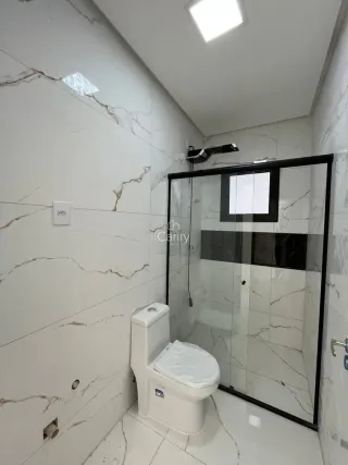 Foto interna de um banheiro com revestimento em mármore branco e box de vidro.