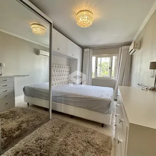 Quarto com cama, armários brancos e janela com cortinas.