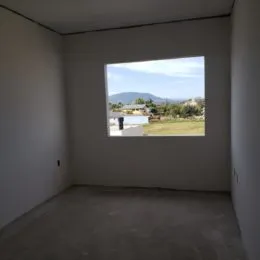 Foto de um cômodo interno com paredes brancas e uma grande janela mostrando a paisagem externa.