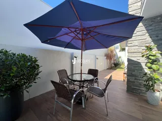 Área externa com mesa e cadeiras de vime sob um guarda-sol azul.